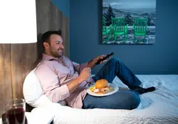 man watching tv on bed with food in hotel room